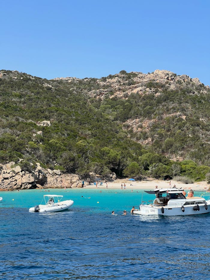 Breathtaking view of a serene beach in Sardinia, Italy, featuring boats and clear turquoise waters.